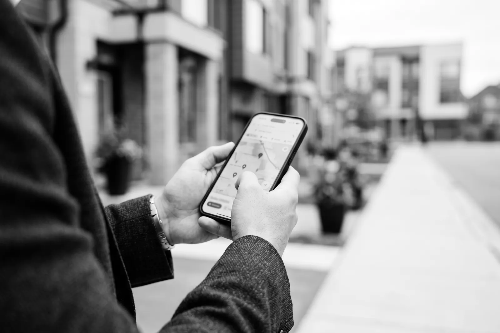 Hands holding a phone with a map on a neighbourhood sidewalk