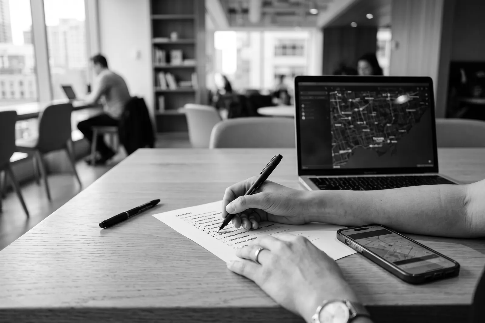 Hands marking a printed checklist beside a laptop and phone