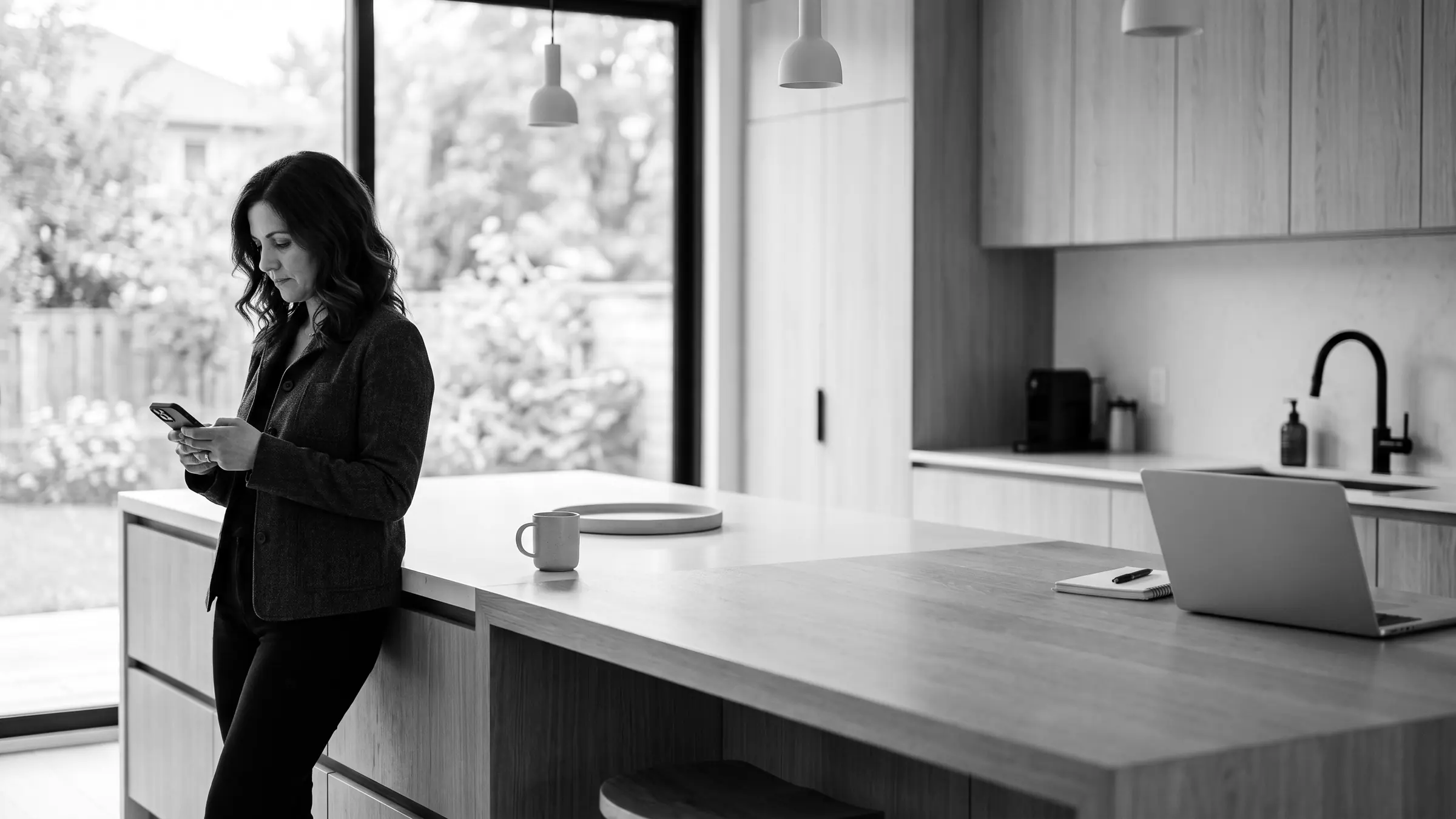 A business owner checking her phone at a kitchen island, laptop open