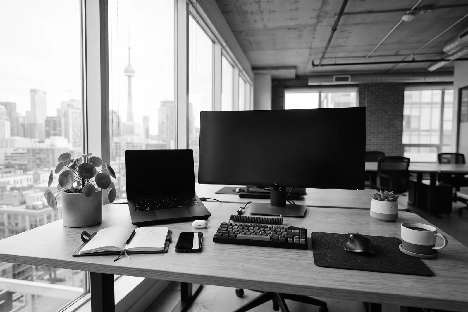 Agency desk with a laptop and monitor by a window overlooking the Toronto skyline